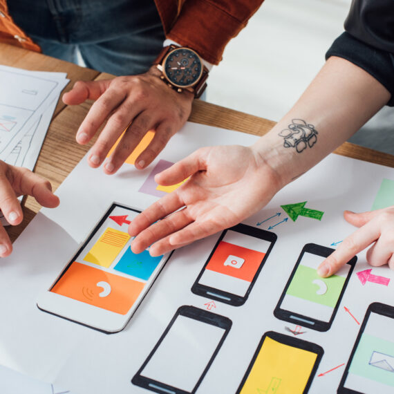 Cropped view of ux designers working with sketches and mobile wireframe layouts at table